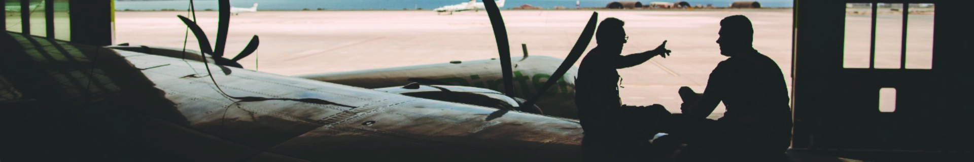 Immagine in controluce di due operai e di un ATR nell'hangar di Binter
