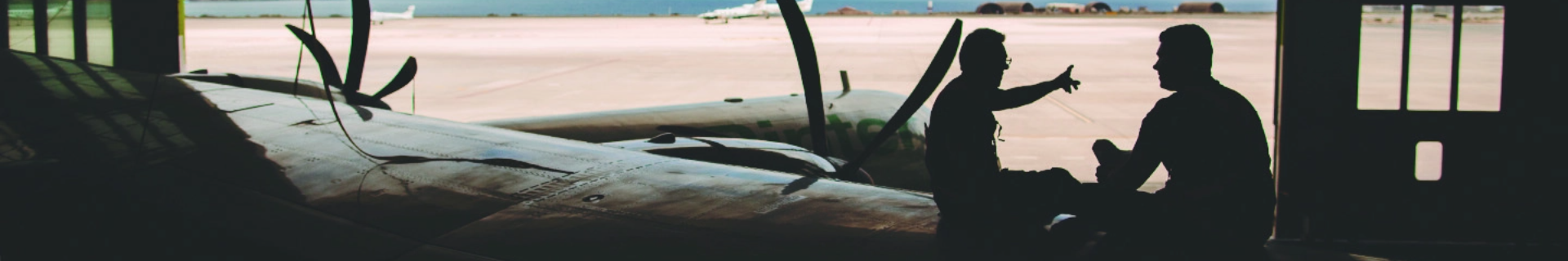 Backlit image of two workers and an ATR in the Binter hangar