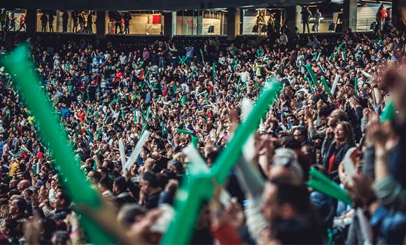 Excited audience waving green inflatable sticks at an event.