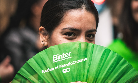 Woman holding a green fan with the Binter logo in front of her face.