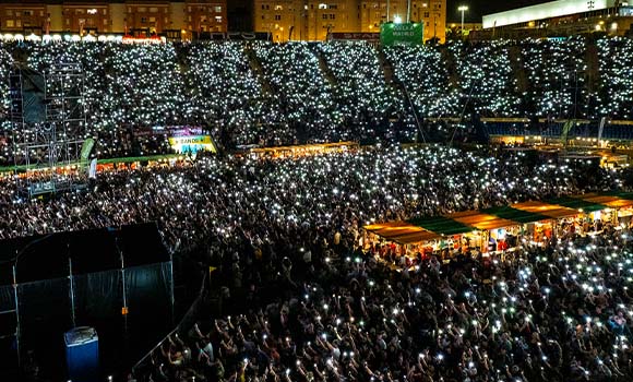 Stadium full of people with phone lights on during a night concert.