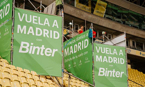 Green banners promoting flights to Madrid with Binter airline in a stadium.