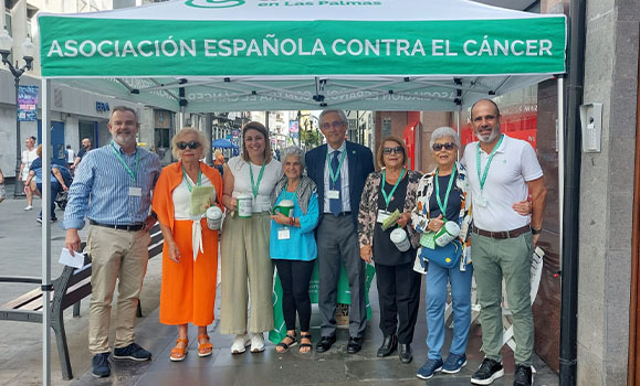 Group of people under a Spanish Association Against Cancer tent on the street.