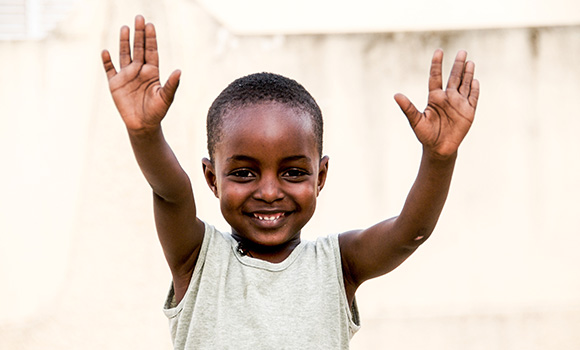 A child smiling while raising his hands in the air