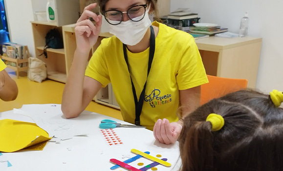 Voluntaria con mascarilla realiza una actividad manual con una niña.
