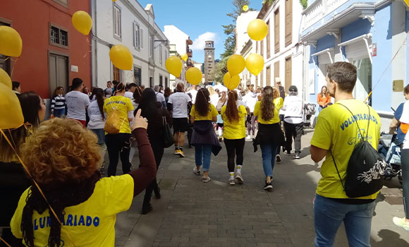 Personas en una caminata por la calle con globos amarillos.