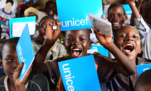 Um grupo de crianças sorridentes com pastas da Unicef.