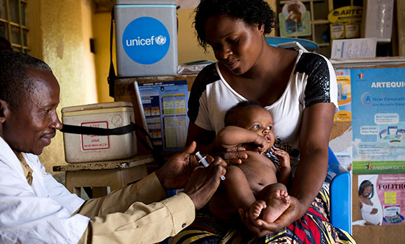 Um médico da Unicef examina uma criança enquanto a sua mãe o abraça.