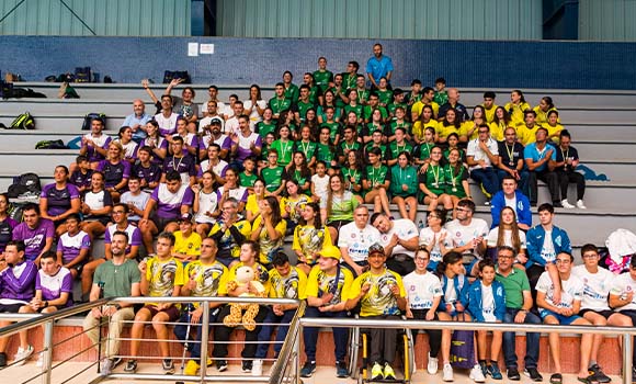 Large group of people, mostly young, organized on bleachers, wearing different colored shirts.