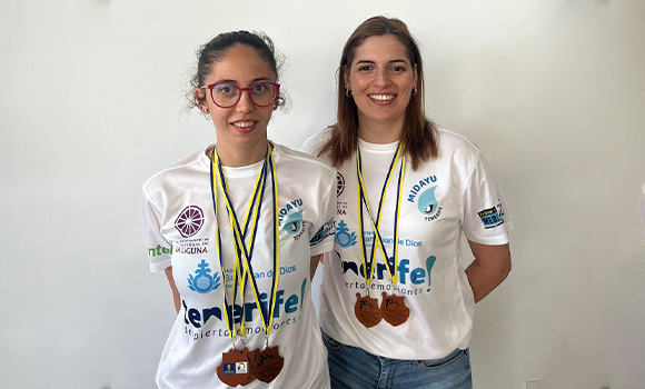 Two young women in white shirts, smiling and displaying their medals.