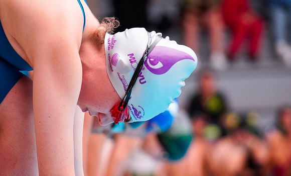 Swimmer with a white and purple swim cap, focused before competing.